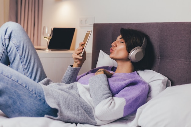 Free photo happy woman at home on comfy bed wearing warm clothes pullover, listen music