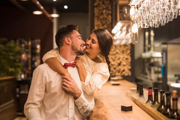 Happy woman hugging cheerful man at bar counter 