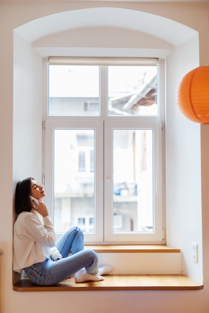 Free photo happy woman is talking on phone while sitting near the window