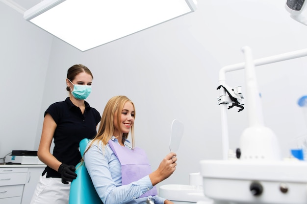 Happy woman looks at her teeth in the mirror sitting at the dentist office