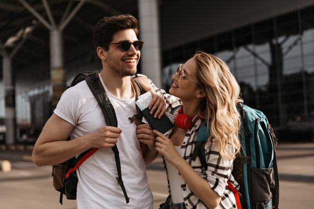 Happy woman in plaid shirt and man in white tee smiles near airport