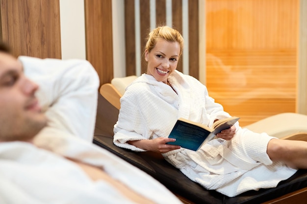 Happy woman reading a book while spending a relaxing day wit her husband at wellness center