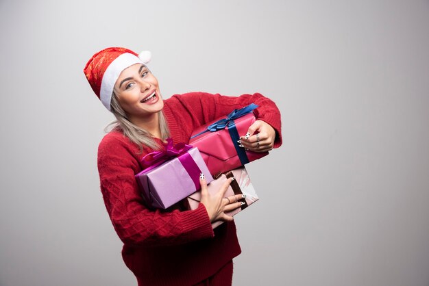 Happy woman in Santa hat holding bunch of gift boxes.