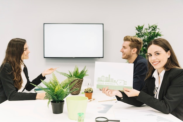 Happy woman showing energy saving concept on paper in office