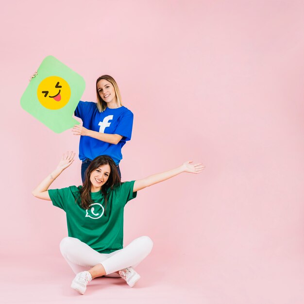 Happy woman sitting in front of her friend with winking emoji speech bubble