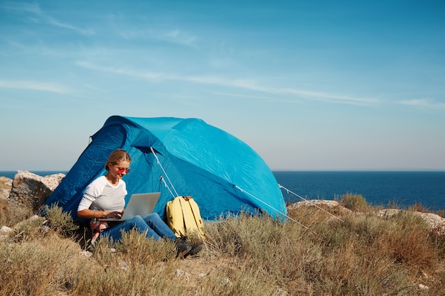 Free Photo happy woman sitting near tent with laptop