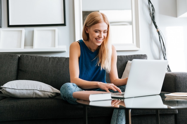 Happy woman sitting on sofa and using laptop at home