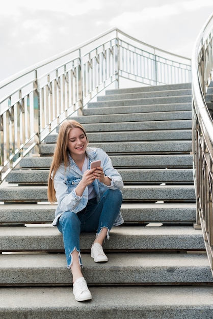 Happy woman sitting on staircases and using smartphone