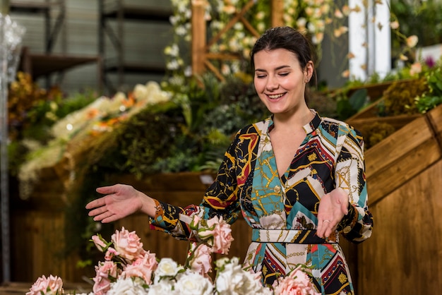 Happy woman standing near roses in green house