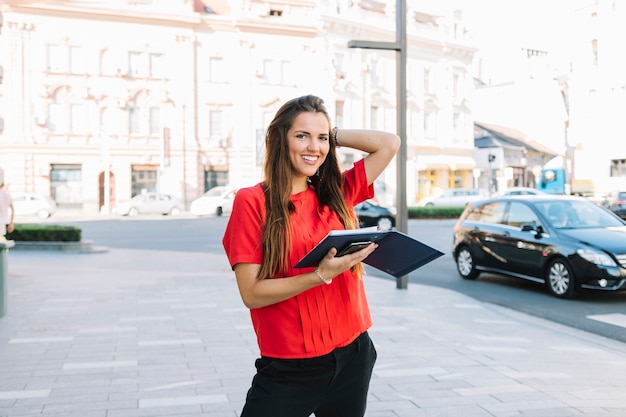 Happy woman standing on sidewalk holding diary