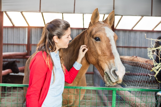 Happy woman stroking the horse in the stable