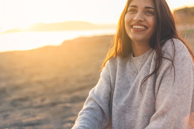 Happy woman in sweater sitting on sandy sea shore