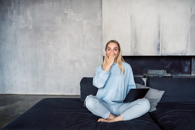 Happy woman using silver laptop while sitting on sofa