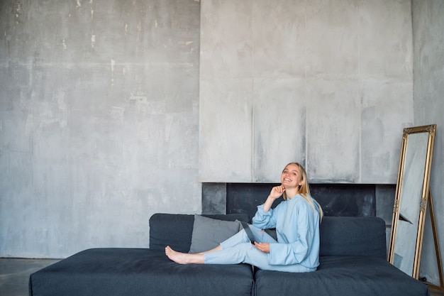 Free photo happy woman using silver laptop while sitting on sofa