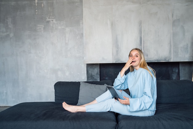 Happy woman using silver laptop while sitting on sofa