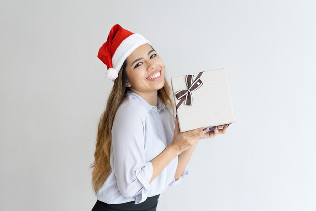 Happy woman wearing Santa Claus hat and holding gift box