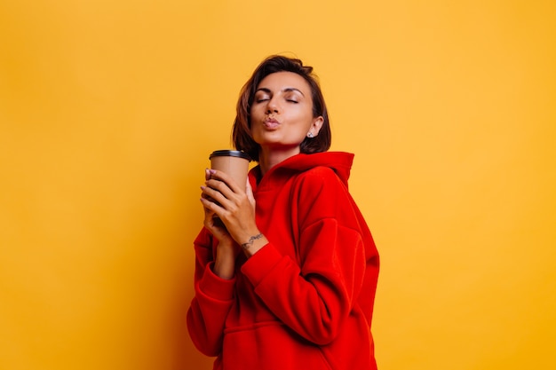 Happy woman wearing warm winter clothes warms herself with cup of hot coffee