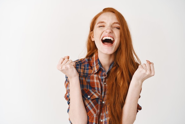 Free photo happy woman winning scream of joy and triumph redhead girl achieve goal and celebrating shouting for rejoice standing over white background