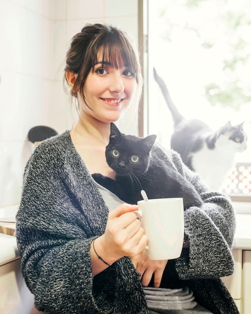 Free Photo happy woman with cup of coffee holding her cat