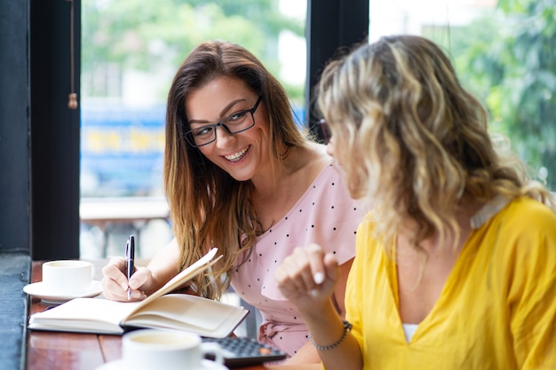 Happy women drinking coffee and working in cafe