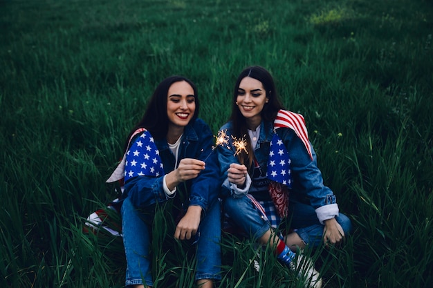 Happy women sitting on grass with Bengal lights 