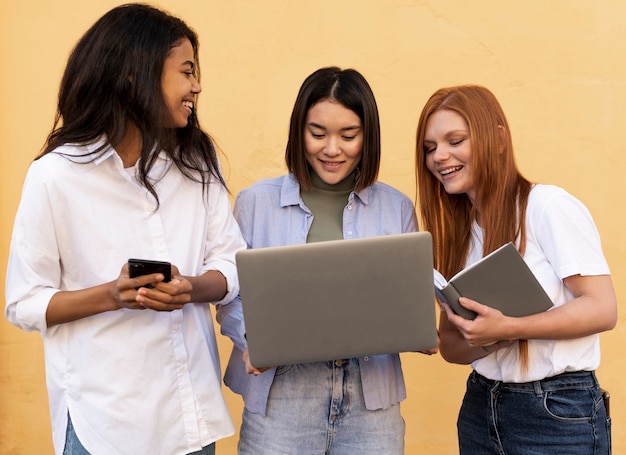 Happy women using different objects in front of a yellow wall