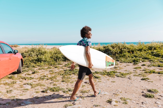 Free photo happy young african american male coming with surfboard along seaboard