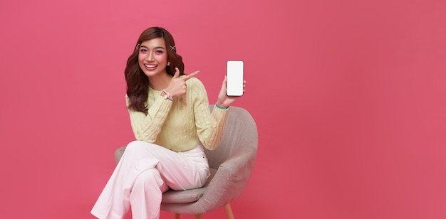 Happy young Asian woman showing empty screen mobile phone While her sitting on chair