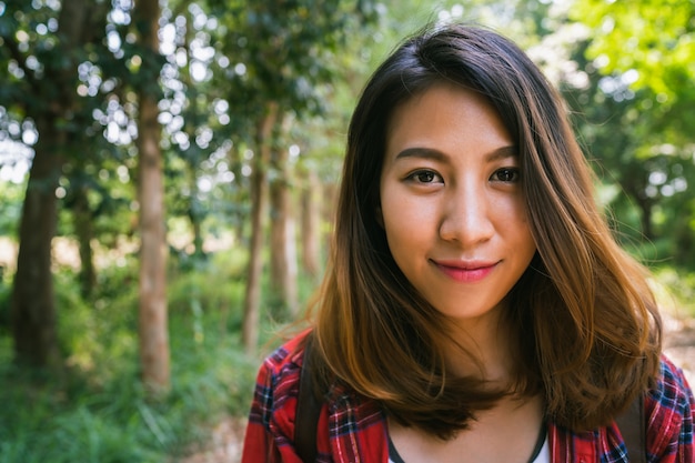 Happy young Asian woman traveler with backpack walking in forest. 