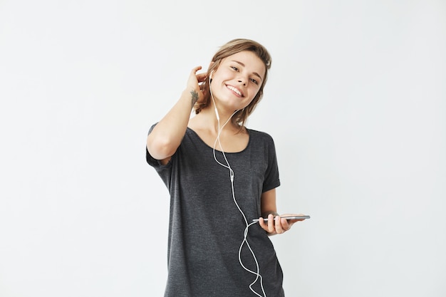 Happy young beautiful girl in headphones holding phone smiling .