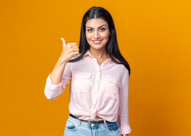 Happy young beautiful woman in casual clothes  smiling confident showing thumbs up standing over orange wall