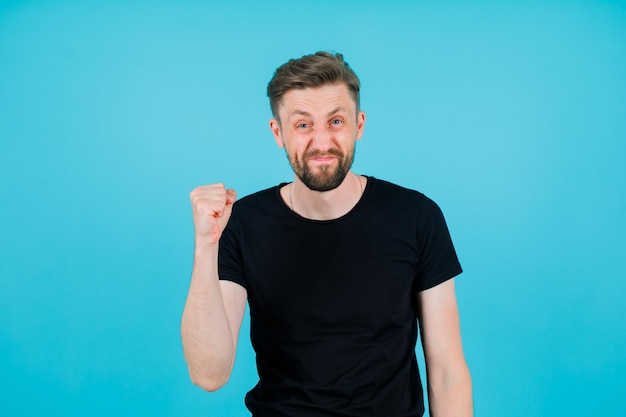 Happy young boy is raising up his fist on blue background