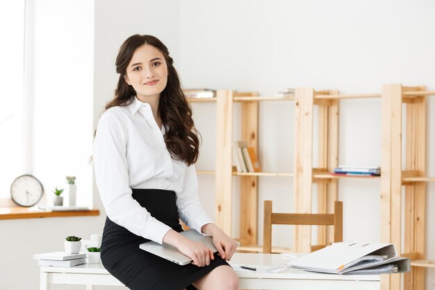 Happy young business woman or secretary holding laptop in modern office