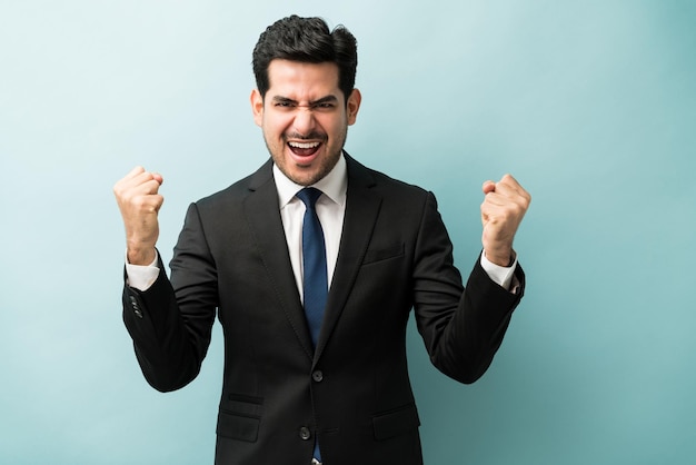 Free photo happy young businessman with clenched fist enjoying good news against colored background