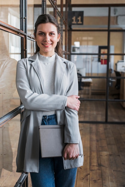 Free photo happy young businesswoman holding diary looking at camera at workplace