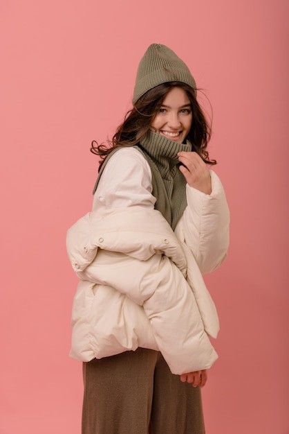 Free Photo happy young caucasian brunette girl in winter clothes smiling at camera on pink background shopping in the cold season