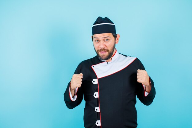 Happy young chef is raising up his fists on blue background