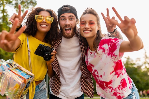 Free photo happy young company of emotional smiling friends walking in park with photo camera, man and women having fun together