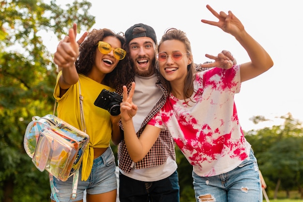 Happy young company of emotional smiling friends walking in park with photo camera, man and women having fun together