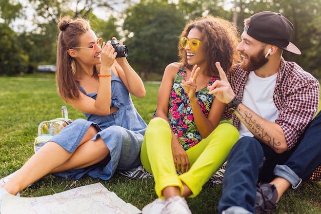 Free Photo happy young company of friends sitting park, man and women having fun together, colorful summer hipster fashion style, traveling taking photo on camera, talking, smiling