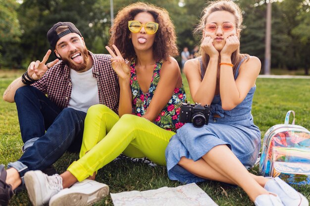 Happy young company of friends sitting park, man and women having fun together, traveling with camera, funny emotional