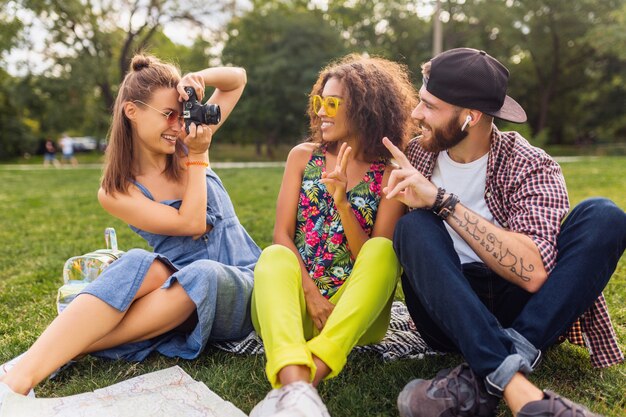 Happy young company of friends sitting park, man and women having fun together, traveling with camera, taking pictures