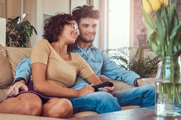 Happy young couple cuddling while watching TV in their living room.