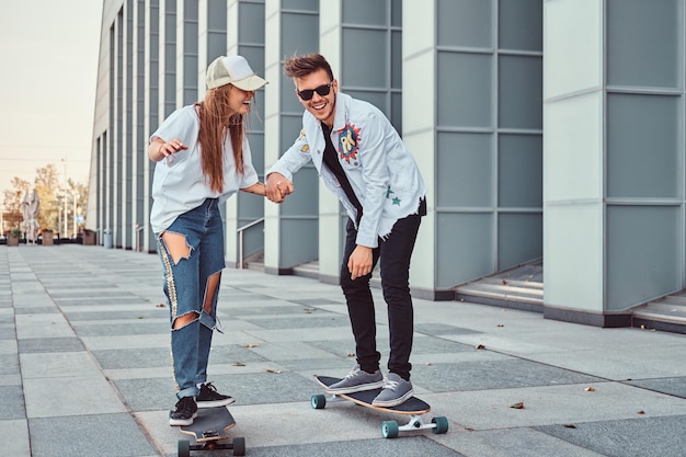 Free photo happy young couple having fun while driving skateboards on the modern street.