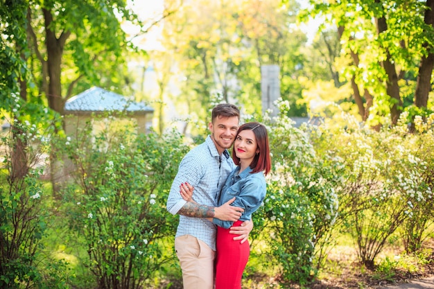 Happy young couple at park standing and laughing on the bright sunny day