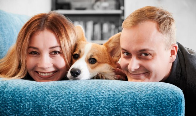 Happy young couple resting on couch with cute Corgi dog