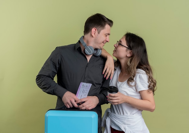 Happy young couple of tourists man and woman holding suitcase looking at each other smiling over light