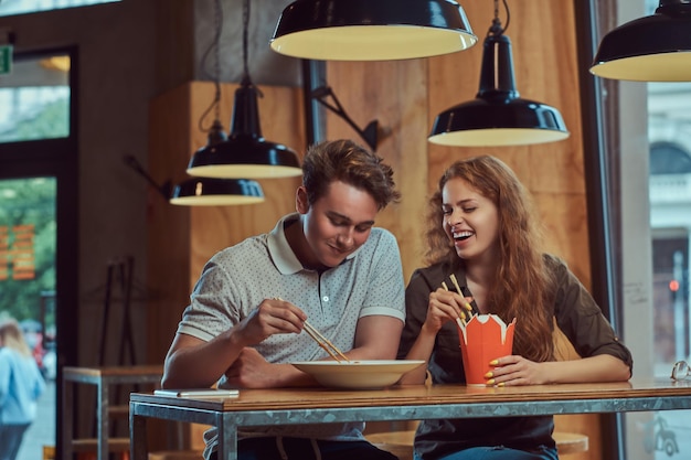 Free photo happy young couple wearing casual clothes eating spicy noodles in an asian restaurant.