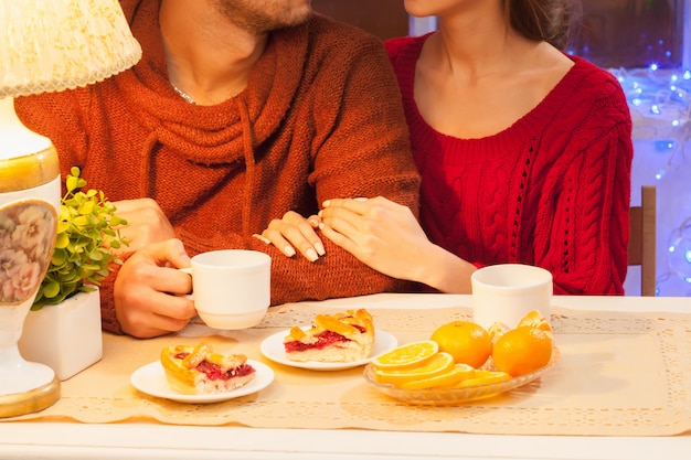 The happy young couple with cups of tea and cakes.