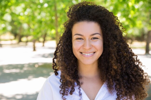 Happy young curly-haired lady posing at camera in park